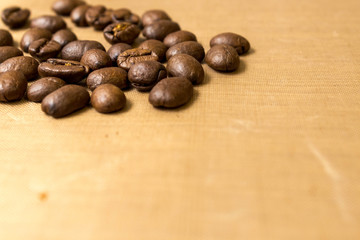 Beige background with coffee beans. Roasted Arabica coffee beans scattered on a beige textured background like flax close up with copy space