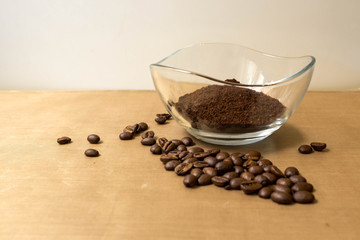 Coffee background. Natural roasted coffee beans and ground coffee in a glass transparent bowl on a natural beige fabric background on the table, side view from Kopi space