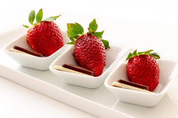 Three fresh red strawberries with chocolate in small white bowls