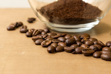 Coffee background. Natural roasted coffee beans and ground coffee in a glass transparent bowl on a natural beige fabric background on the table, side view from Kopi space