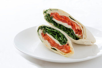 Wrap - stuffed pancake with smoked salmon, goat cheese and romaine lettuce on a white plate