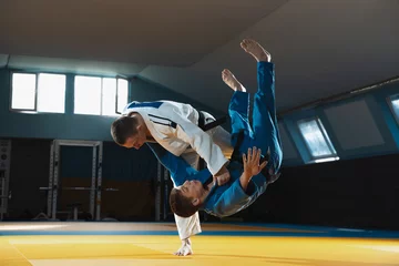 Two young judo caucasian fighters in white and blue kimono with black belts training martial arts in the gym with expression, in action, motion. Practicing fighting skills. Overcoming, reaching target © master1305
