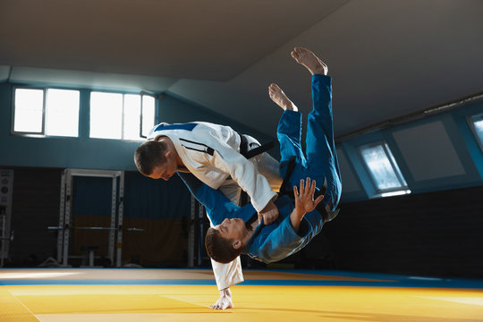 Two young judo caucasian fighters in white and blue kimono with black belts training martial arts in the gym with expression, in action, motion. Practicing fighting skills. Overcoming, reaching target - Powered by Adobe