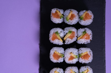 Maki sushi set with salmon and avocado on a slate plate and purple background. Japanese cuisine. Copy space.