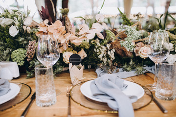 festive wooden tables decorated with compositions of flowers and greenery, on the tables are plates with napkins, glasses and candles