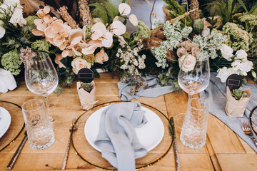 festive wooden tables decorated with compositions of flowers and greenery, on the tables are plates...