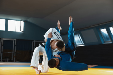 Two young judo caucasian fighters in white and blue kimono with black belts training martial arts...