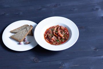 Red beetroot soup borsch in white plate with bread and garlic on black wooden table