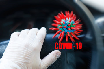 Red headline with inscription COVID-19, abstract virus strain model sitting on the steering wheel of a vehicle and human hand in medical gloves. Concept of attention about spread Coronavirus COVID-19.