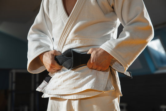 Young judo caucasian fighter in blue kimono with black belt posing confident in the gym, strong and healthy. Practicing martial arts fighting skills. Overcoming, reaching target, self building up.