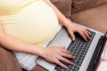 Fototapeta premium Portrait of a beautiful pregnant woman working at home using a computer