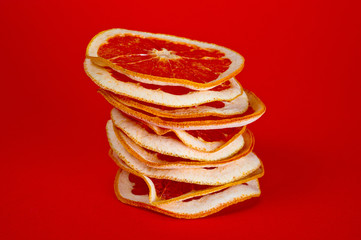 Chips of dried grapefruit sliced in thin circles, shot on a red background. Background for vegetarianism, healthy and wholesome food.
