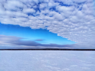 Winter landscape. Blue sky with white clouds over a snowy lake