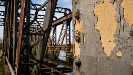 Focus on flaking paint on an iron and rivets beam with old bridge in background
