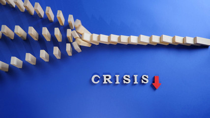 Crisis word with red arrow and falling wooden blocks with domino effect on a blue background....