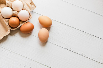 Brown and white organic chicken eggs in a brown paper box placed on a white wooden table. Eggs provide protein, suitable for health lovers.
