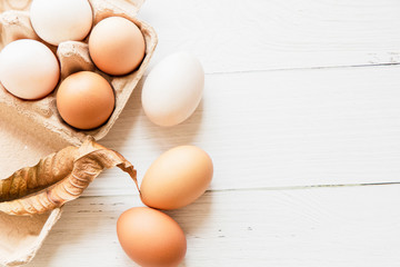 Brown and white organic chicken eggs in a brown paper box placed on a white wooden table. Eggs provide protein, suitable for health lovers.