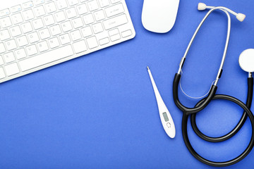 Stethoscope with thermometer, keypad and mouse on blue background