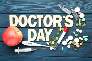 Text Doctor's Day with colorful pills and medicine instruments on blue wooden table