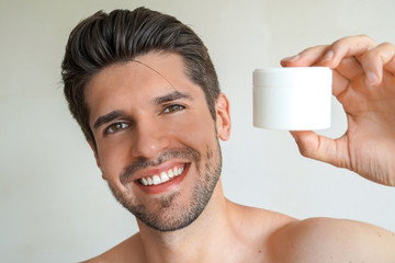 Young handsome man with a perfect skin and hair is showing a product in his bathroom with a wide smile 