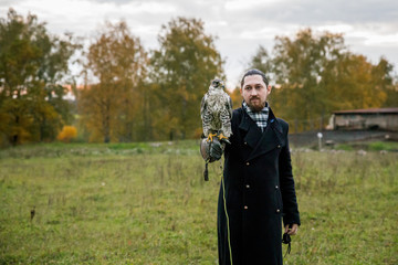 The concept of falconry. A man of European appearance with beard, with a leather glove and a beautiful hawk on his hand