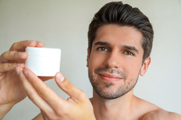 Young handsome man with a perfect skin and hair is showing a product in his bathroom 