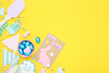 Easter concept. Greeting card with eggs, paper flags, marshmallows and sprinkles on yellow background