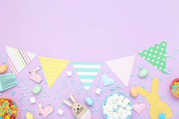 Easter concept. Paper flags with rabbits, sprinkles and marshmallows on purple background