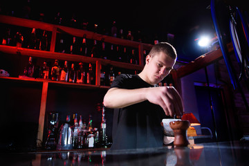 Barman fills black burnt ceramic bowl for hookah smoking different types of tobacco.