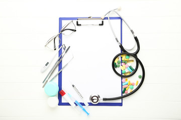 Doctor's Day concept. Colorful pills with medicine instruments and clipboard on white wooden table