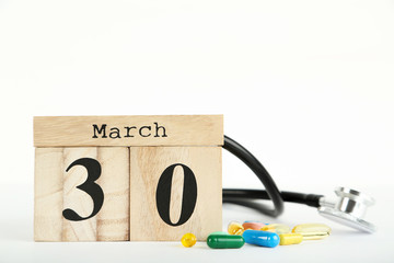Doctor's Day concept. Cube calendar with colorful pills and stethoscope on white background