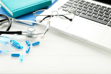 Doctor's Day concept. Blue pills with stethoscope, eyeglasses and computer on white wooden table