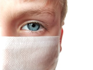 Face of a handsome white seven year old boy in a white protective surgical mask. Eye with a light gray iris. Half face. Blonde hair. White background. Isolate Protection against bacteria and viruses