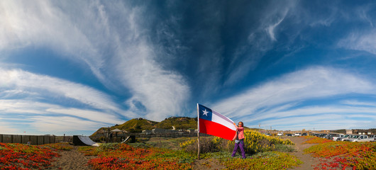 Panorama with mountains and clouds in the foreground a girl with the Chilean flag. Photographed through a polarizing filter