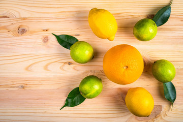 orange, two lemons and four limes lie on a wooden surface with green leaves