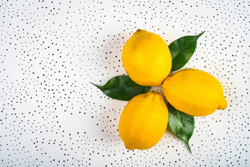 three lemons with green leaves are dotted on a white surface.