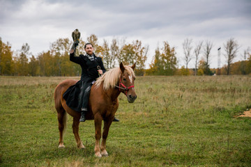 Fototapeta premium The concept of falconry. A man with a leather glove and a beautiful Falcon on handon a chestnut, red, and red horse
