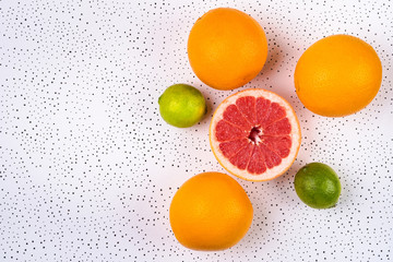 three whole oranges, two limes and half grapefruit are dotted on a white surface.