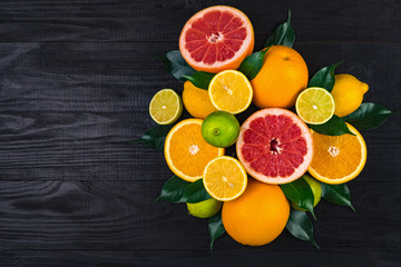 citrus fruits, grapefruits, lemons, oranges, limes with green leaves lie on a brown wooden table. view from above