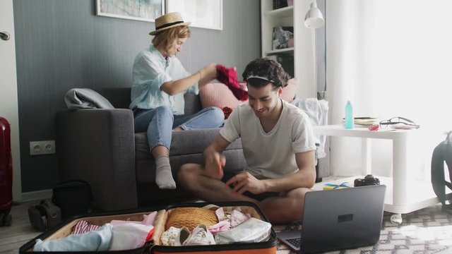 Girl in a hat on the couch and a guy with a laptop sorting things out on a trip