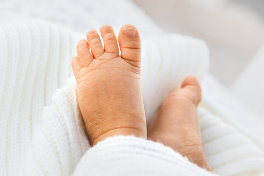 Closeup of newborn baby girl leg on a white blanket, infant barefoot in a selective focus