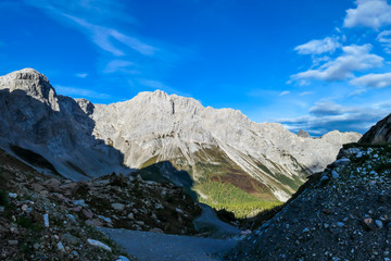 Obraz premium A pathway leading to high peaks in Italian Alps. Sharp slopes on both sides of the valley. Hard to reach mountain peaks. There are many mountain ranges in the back. Serenity and peace. Autumn vibes