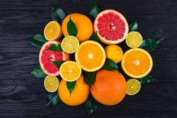 Fototapeta na wymiar fruits, half grapefruits, lemons, oranges, limes with green leaves lie on a brown wooden table