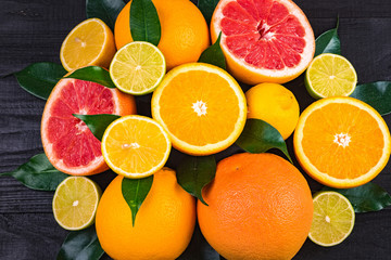 fruits, half grapefruits, lemons, oranges, limes with green leaves lie on a brown wooden table, half.