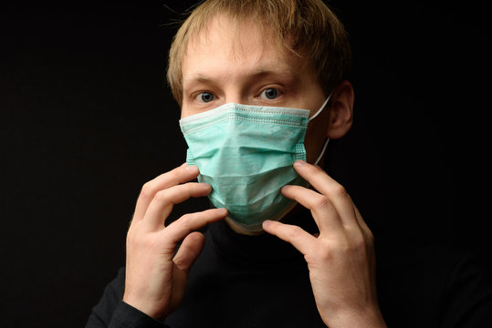 Young Woman Wearing Medical Mask Protecting From Virus. Serious Female With Sad Eyes Touching Protection Mask From Dangerous Coronavirus Epidemic And Looking At Camera On Black Background