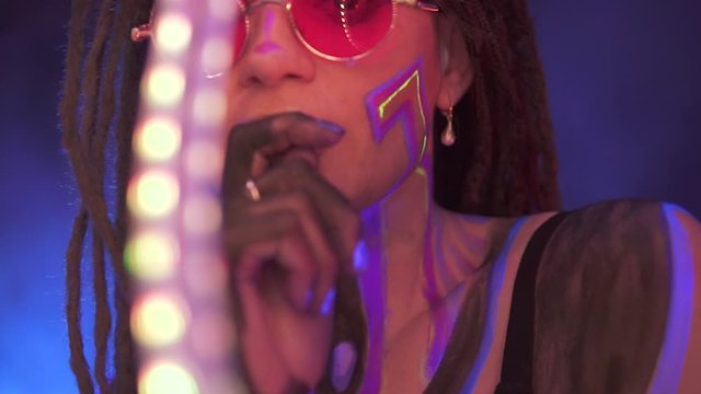 Portrait of a Girl with Dreadlocks in Neon UF Light. Model Girl dancing with a LED lent is Red Sunglasses, Art Design of Female Disco Dancer Model in UV, Colorful Abstract Make-Up.