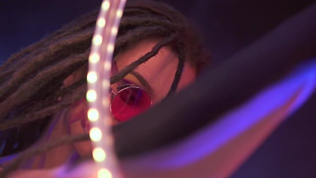 Portrait of a Girl with Dreadlocks in Neon UF Light. Model Girl dancing with a LED lent is Red Sunglasses, Art Design of Female Disco Dancer Model in UV, Colorful Abstract Make-Up.