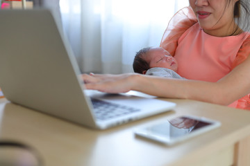 mother parenting a baby newborn sleeping in home office, businesswoman typing keyboard laptop computer of woman working freelance business