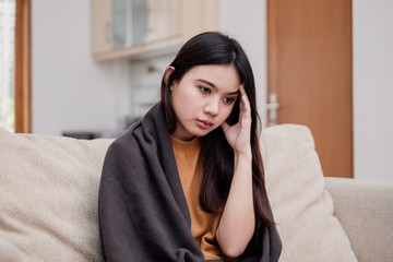 Obraz premium Portrait of Young woman sitting on a couch, holding her head, having a strong headache. Pandemic 2019 Coronavirus 2019-nCoV Concept.