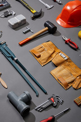 high angle view of tool belt, hammers, monkey wrench, putty knife, pliers, helmet, pipe connector, calipers, angle keys and brush on grey background
